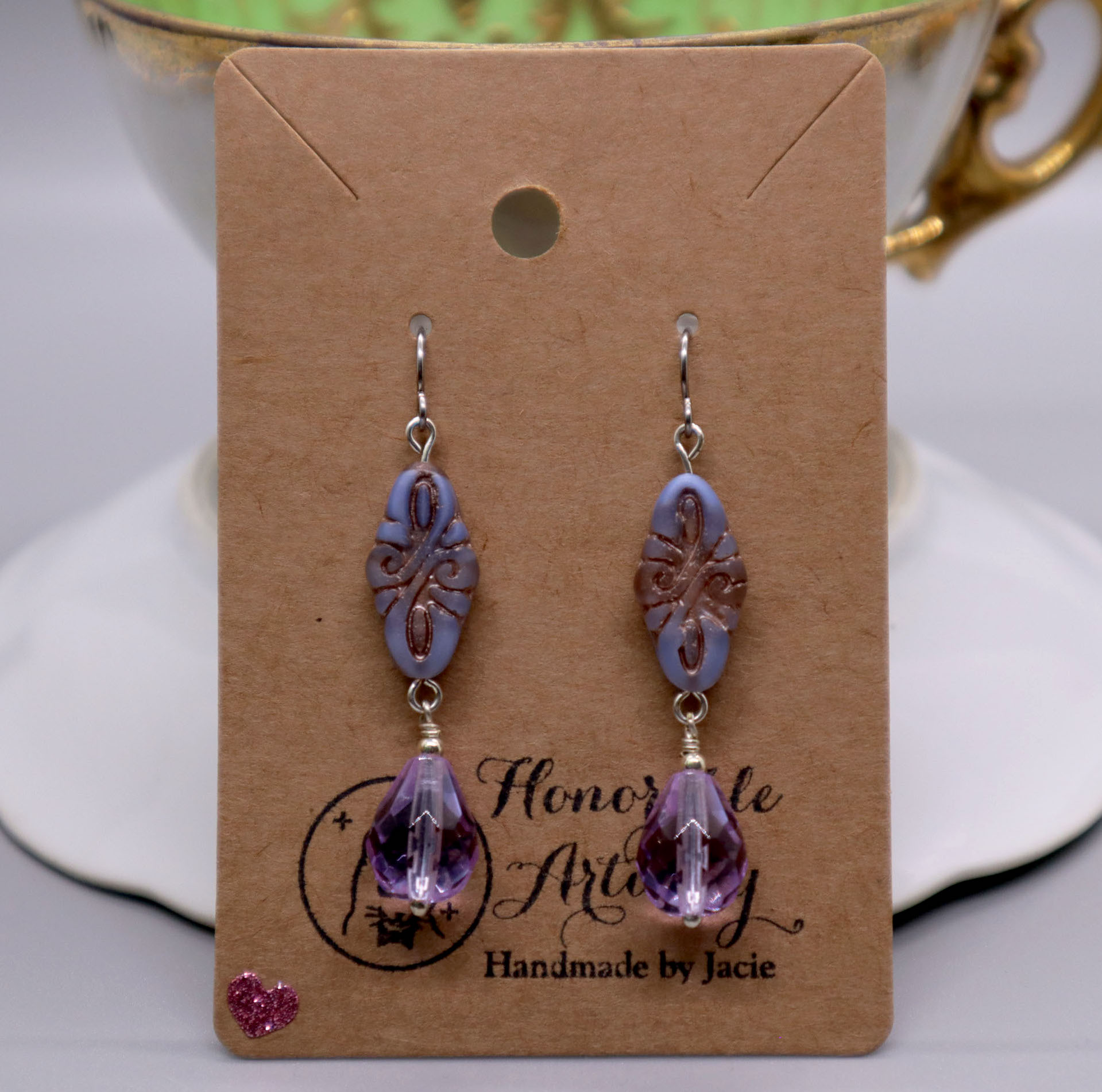 Purple earrings on a earring card displayed sitting on a teacup.