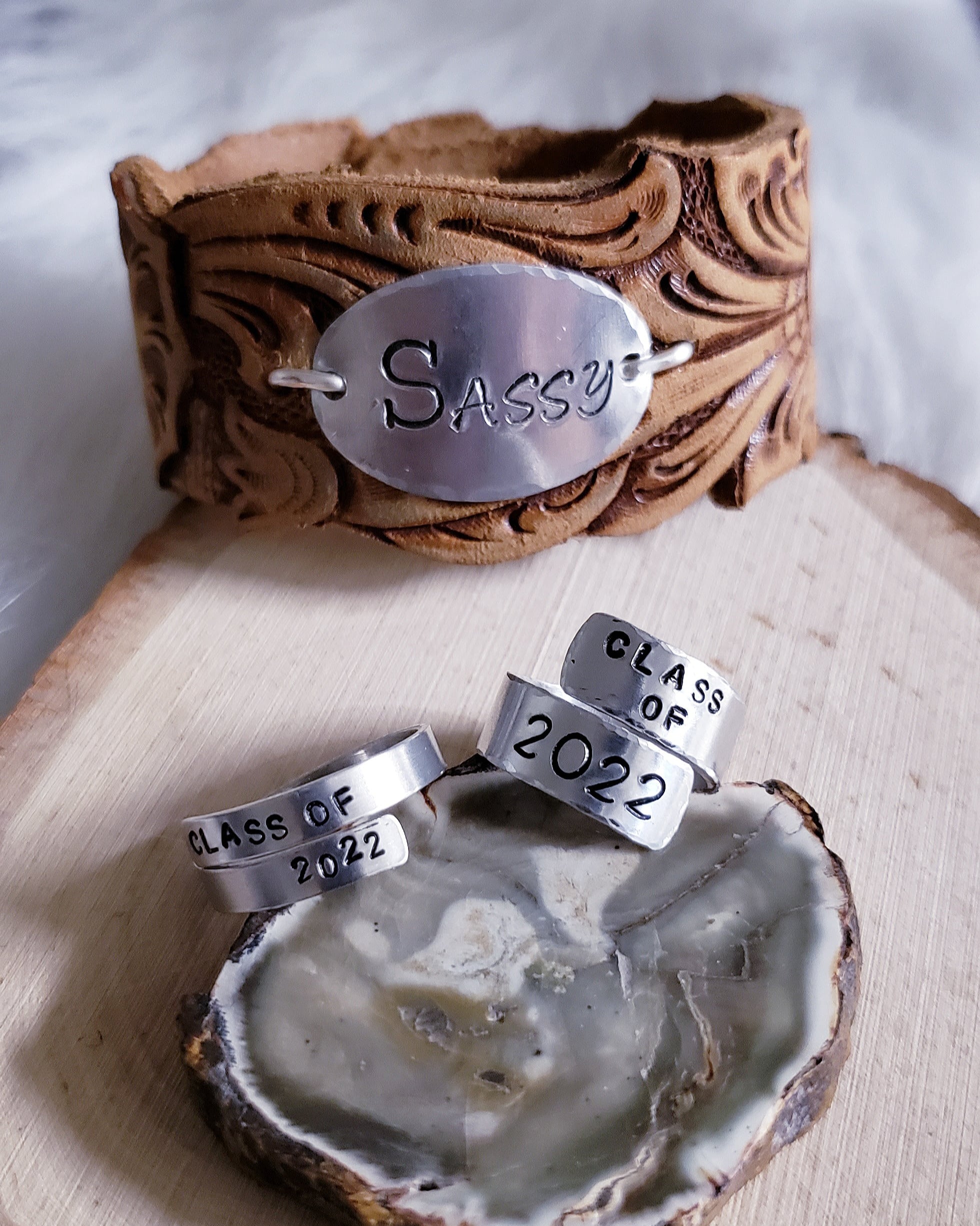 Leather cuff and metal stamped rings, displayed on a wooden board made by Quirky Rose Design.