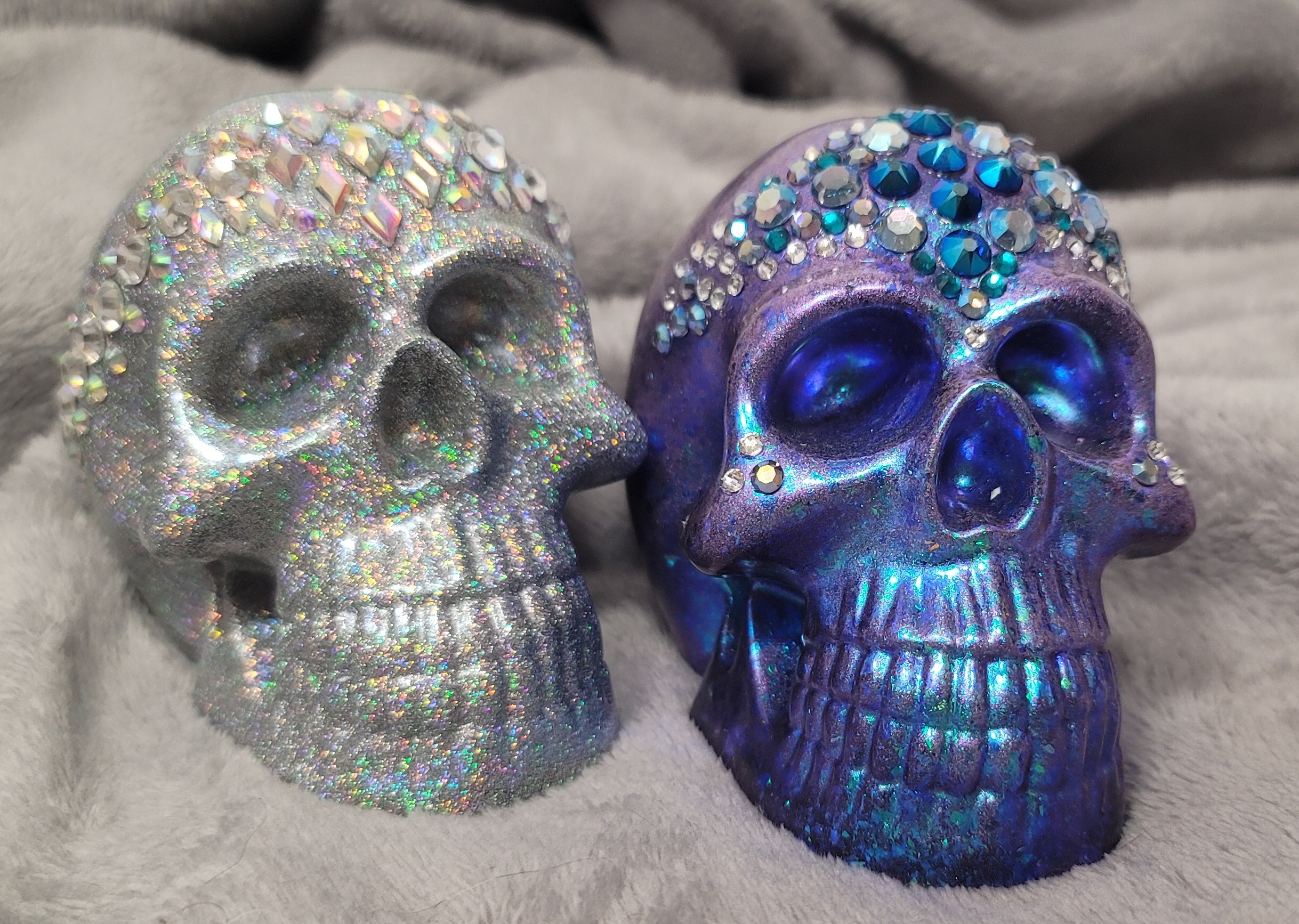 Two resin skulls, one silver with sparkles and one is blue with sparkles.