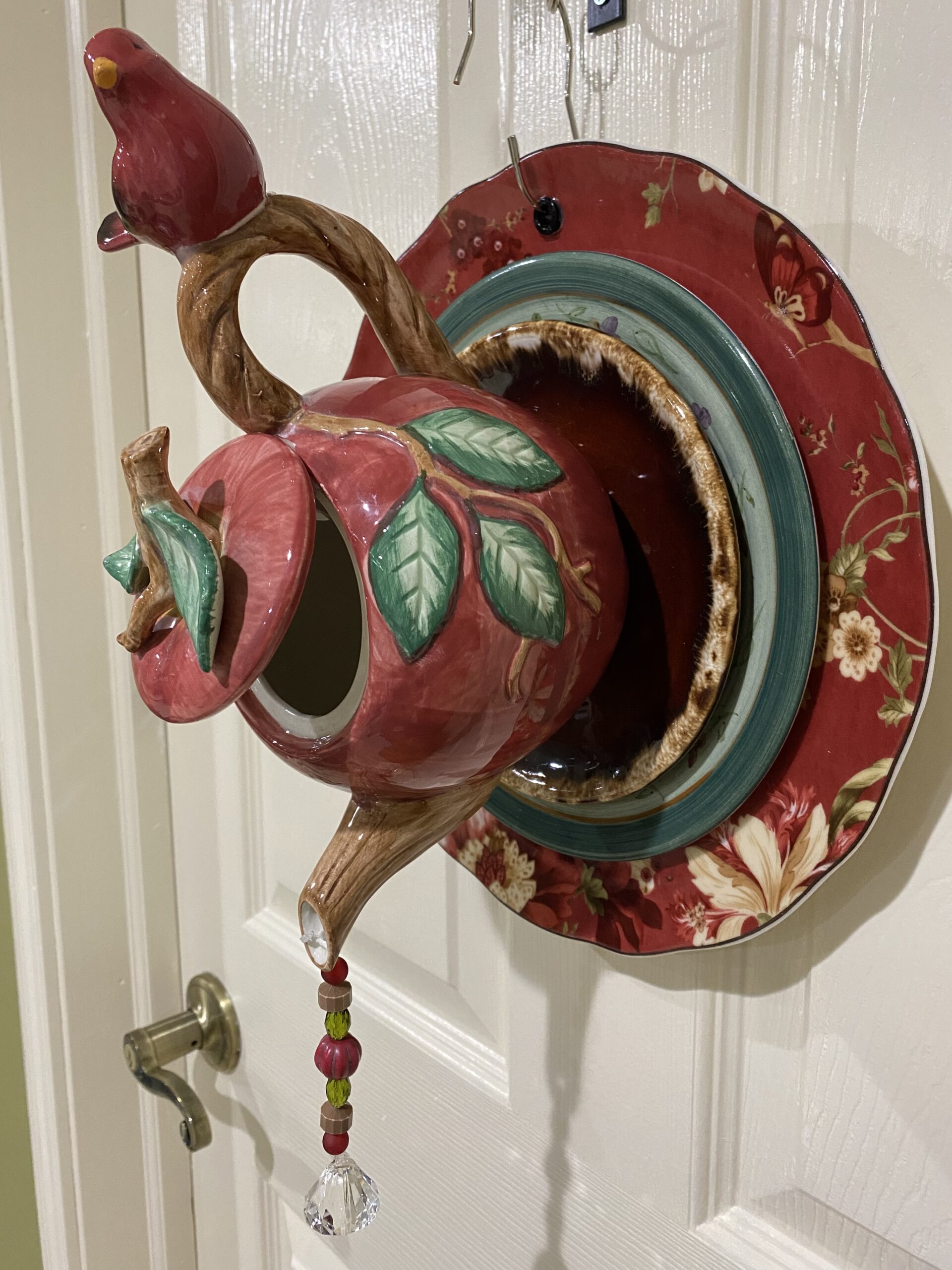 Red teapot now made into garden decoration with cardinal sitting on handle and crystals coming out of the spout.